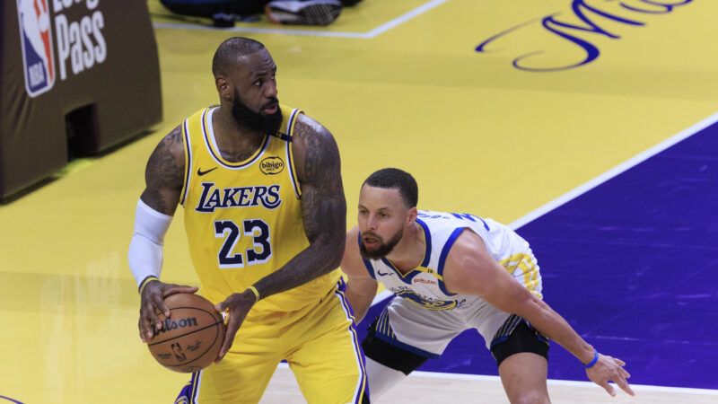 LeBron James holding a basketball, with his back turned to Stephen Curry, who is crouched down low guarding LeBron. | Ariana Ruiz/ZUMAPRESS/Newscom
