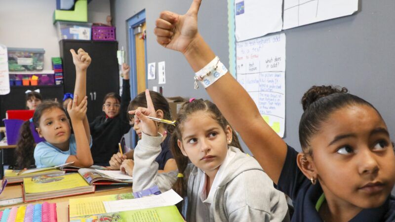 Kids raise their hands as they sit around a table in a classroom | Douglas R. Clifford/ZUMA Press/Newscom