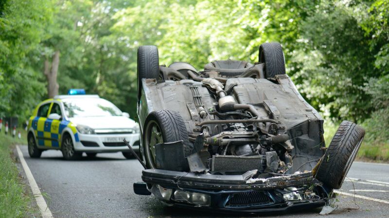 A car is flipped upside down on a rural two-lane road, while a police cruiser is parked on the road a few feet away. | Robert Hyrons | Dreamstime.com