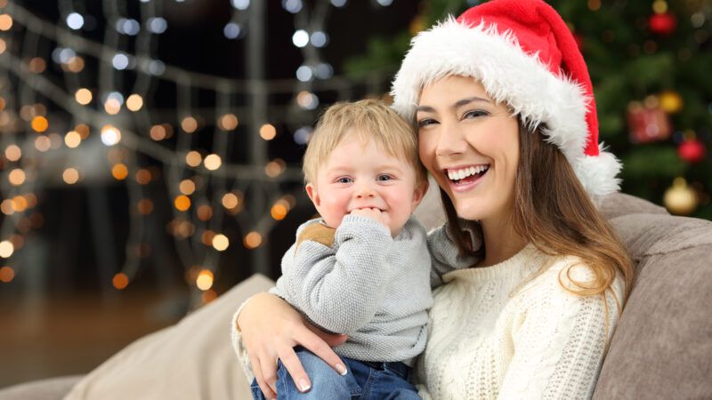 A young woman wearing a Santa hat smiles while holding her toddler son close. | Antonio Guillem | Dreamstime.com