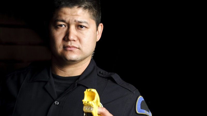 A male police officer brandishes a Taser that has been deployed. | John Roman | Dreamstime.com