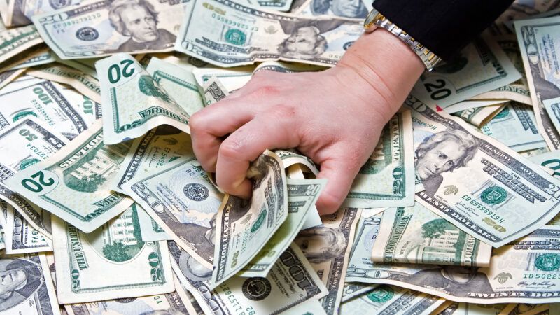 A woman's hand grabs a handful of cash from a pile of  bills. | Paul Hakimata | Dreamstime.com