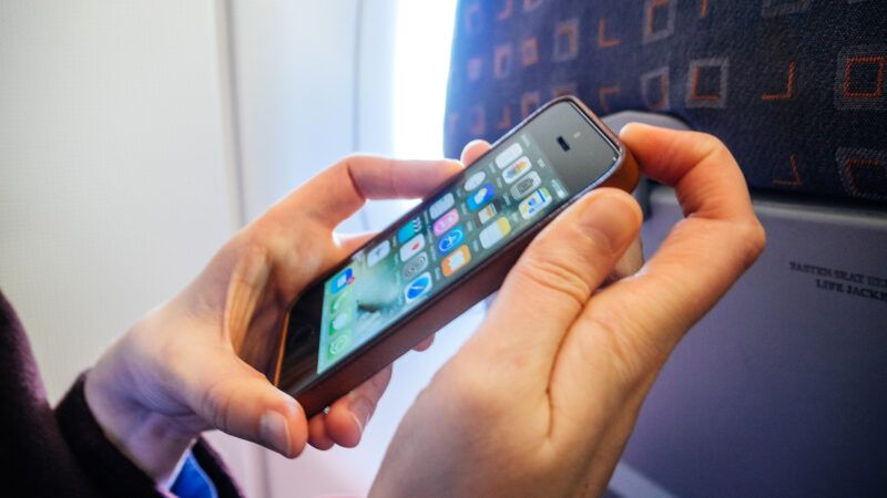 Close-up of a woman's hands as she turns off an iPhone, sitting in an airplane seat. | Ifeelstock | Dreamstime.com