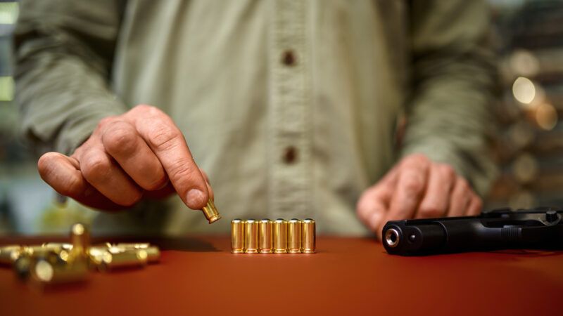 A man in a gun store places bullets onto the counter. | Nomadsoul1 | Dreamstime.com