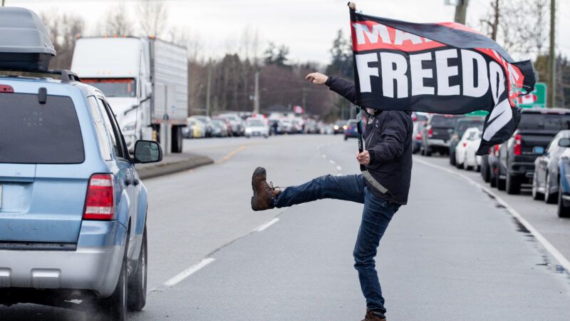 A Freedom Convoy protester marches in the street holding a flag that says "Mandate Freedom." | Ryan Walter Wagner/ZUMAPRESS/Newscom