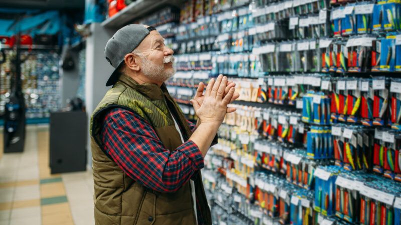 A fisherman happily shops in a bait shop, looking at fish hooks on a retail aisle. | Nomadsoul1 | Dreamstime.com