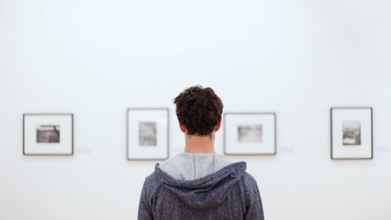 A man, seen from behind, looks at a series of artwork on display in a gallery. | Anyaberkut | Dreamstime.com