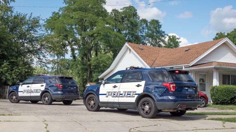 Two police SUVs sit parked outside a residential home. | Lawcain | Dreamstime.com