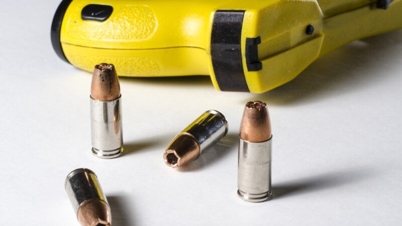 A Taser on its side, next to four hollow-point handgun bullets. | John Roman | Dreamstime.com
