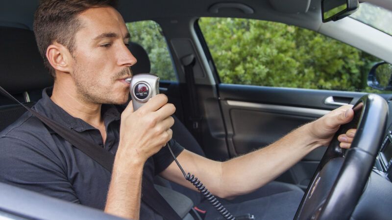 A man sitting in the driver's seat breathes into a breathalyzer hooked up to his ignition. | Zstockphotos | Dreamstime.com