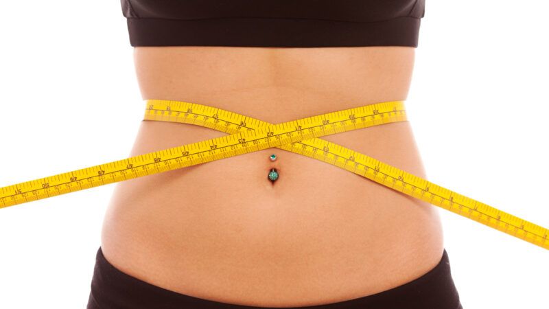 A thin woman in training apparel holds a tape measure cinched around her waist. | Jason Swalwell | Dreamstime.com