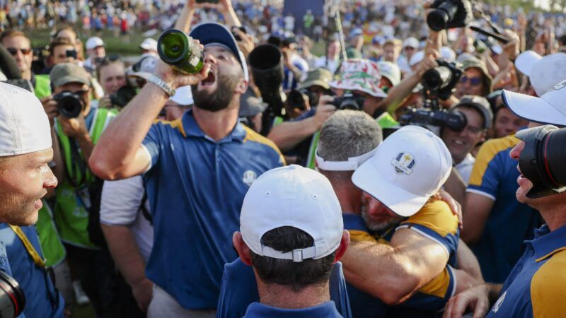 Several men in white hats and blue polo shirts with yellow shoulder stripes hug and celebrate, surrounded by photographers. | News Licensing / MEGA / Newscom/NEWSUK/Newscom