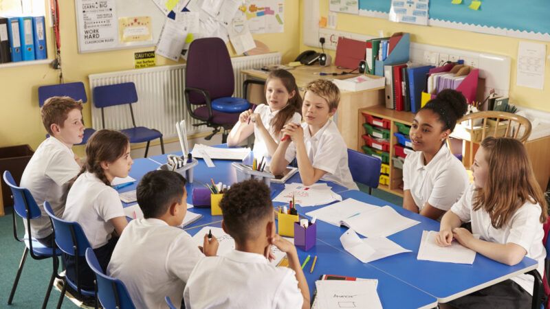 Schoolchildren in a classroom talk as if working on a group project. | Monkey Business Images | Dreamstime.com
