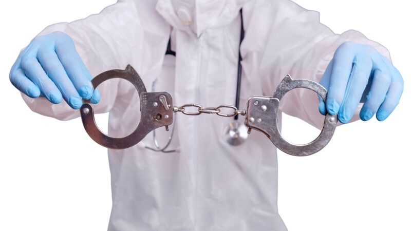 A doctor wearing scrubs and medical gloves holds up a pair of handcuffs. | Andrey Zhuravlev | Dreamstime.com