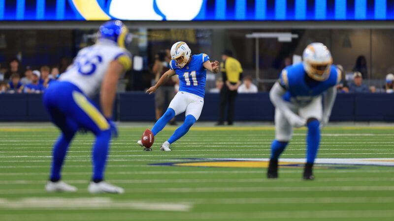 An NFL player in a light blue Chargers uniform kicks off in the background, in focus, while another Chargers player and a Rams player in a white uniform are in the foreground. | Greg Fiore/Icon Sportswire GFR/Greg Fiore/Icon Sportswire/Newscom