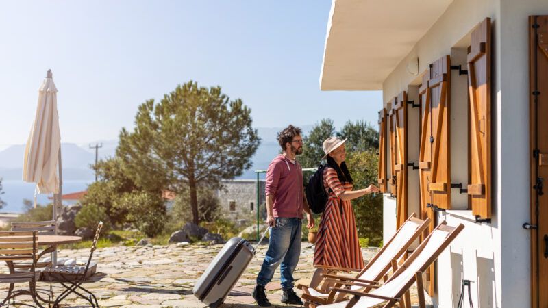 A young couple with suitcases arrives at a beach vacation home. | Piksel | Dreamstime.com