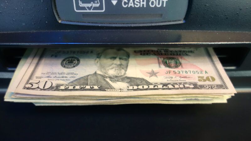 A stack of cash, with a U.S.  bill on top, dispensed out of an ATM. | Bigapplestock | Dreamstime.com