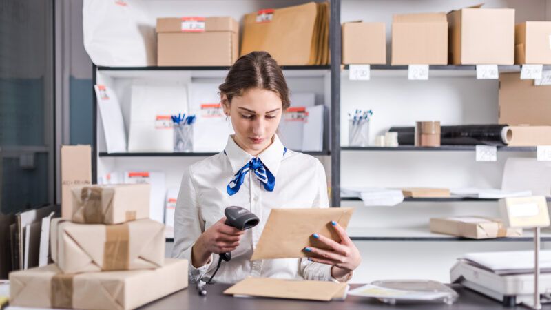 A young woman sits at a desk scanning packages at a post office. | Rlat | Dreamstime.com