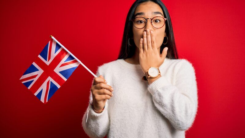 A young woman holds a U.K. flag in one hand while using the other to cover her mouth. | Aaron Amat | Dreamstime.com