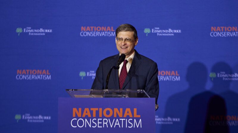 NatCon organizer stands at a podium in front of an orange and blue backdrop to give a speech. | Dominic Gwinn/ZUMAPRESS/Newscom