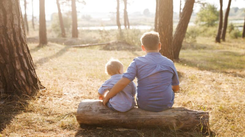 A brother sitting next to his younger sibling outdoors | ID 159417738 ©  Nazarii Karkhut | Dreamstime.com