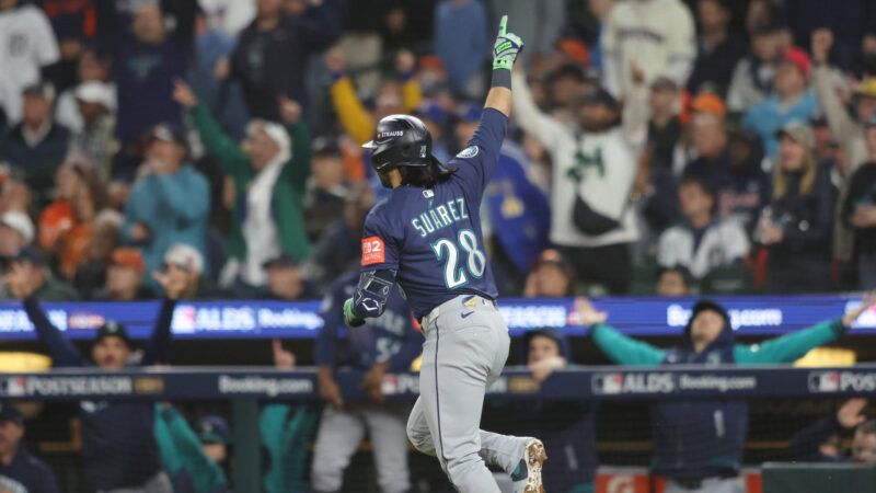 In a navy blue Seattle Mariners jersey, Eugenio Suárez points his hand in the air as he runs to first base, as Mariners players and fans celebrate in the background. | AARON JOSEFCZYK/UPI/Newscom