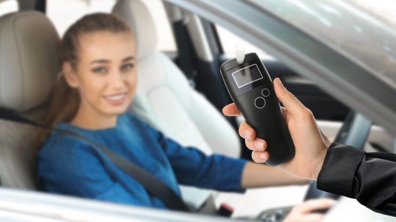 A police officer prepares to administer a breathalyzer to a woman sitting in the driver's seat of her car. A police officer prepares to administer a breathalyzer to a woman sitting in the driver's seat of her car. | Chernetskaya | Dreamstime.com
