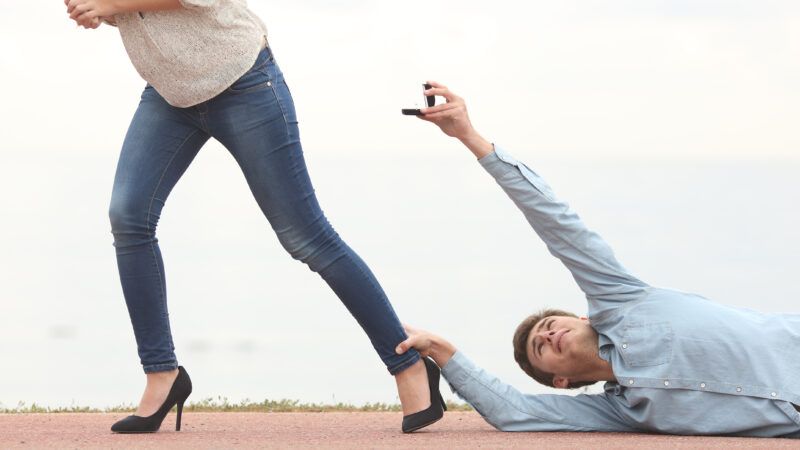 A man lying on the ground holding a woman's foot as she walks away from him. He's holding up an engagement ring. | Antonio Guillem Fernández/Newscom