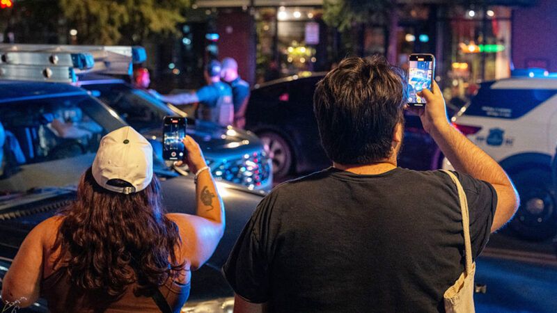 Two people holding phones and recording a police interaction | Photo: Andrew Leyden/Getty