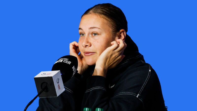 Tennis player Amanda Anisimova sits in front of a microphone and has her fingers in her ears. There's a blue background behind her. | Credit: IMAGO/zhangxiaolei/IMAGO/VCG/Newscom