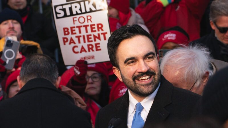 Zohran Mamdani surrounded by other people at a nurses' protest. One of them is holding up a sign that says "On strike for better patient care." | Derek French/ZUMAPRESS/Newscom