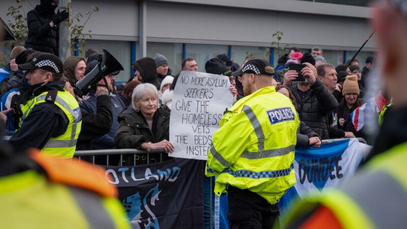 Police in Scotland at a protest outside the Cladhan Hotel. A demonstrator holds a sign that reads, "No more asylum seekers, give the homeless vets the beds instead." | Cameron Scott/ZUMAPRESS/Newscom