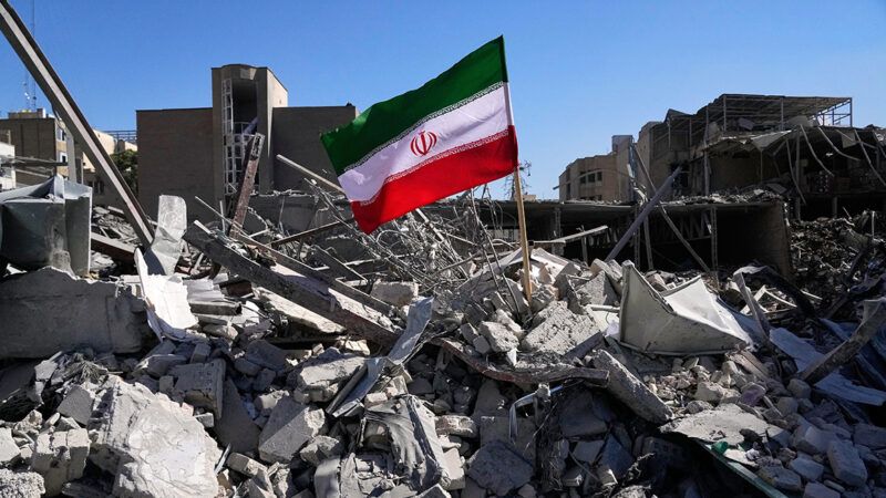 An Iranian flag standing amid a pile of rubble | Photo: Tehran, Iran, on March 3, 2026; Vahid Salemi/Associated Press
