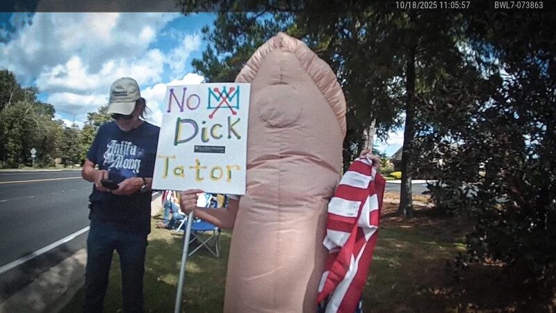 Bodycam footage of Renea Gamble at an October 2025 No Kings protest, wearing an inflatable penis costume and holding a sign that says "No Dick-Tator." | Fairhope Police Department