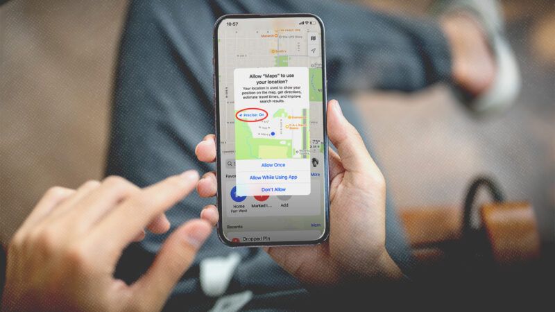 A person holds a cellphone displaying a request for permission to track the phone's location | Envato