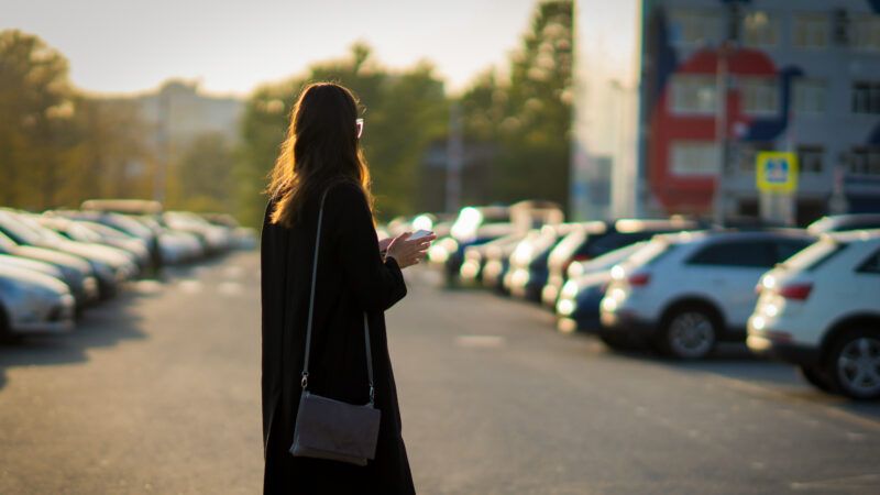 A woman stands, seemingly confused, in the middle of a parking lot full of rental cars. | DPST/Newscom