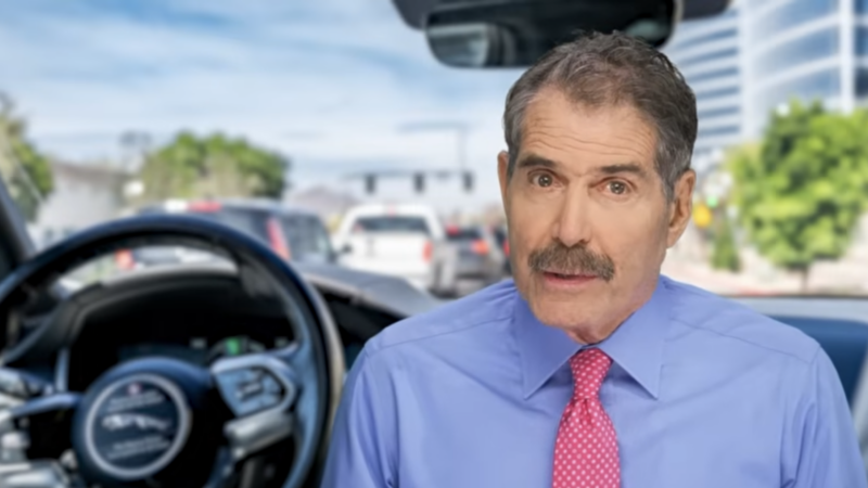 John Stossel is seen next to a steering wheel | Stossel TV