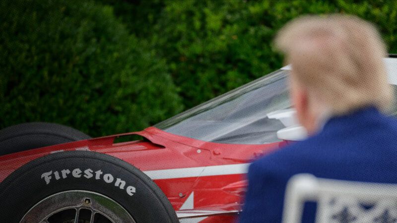 The back of President Donald Trump's head is photographed looking at the front of a red IndyCar, in front of a pair of tall bushes. | Matt Kaminsky/ZUMAPRESS/Newscom