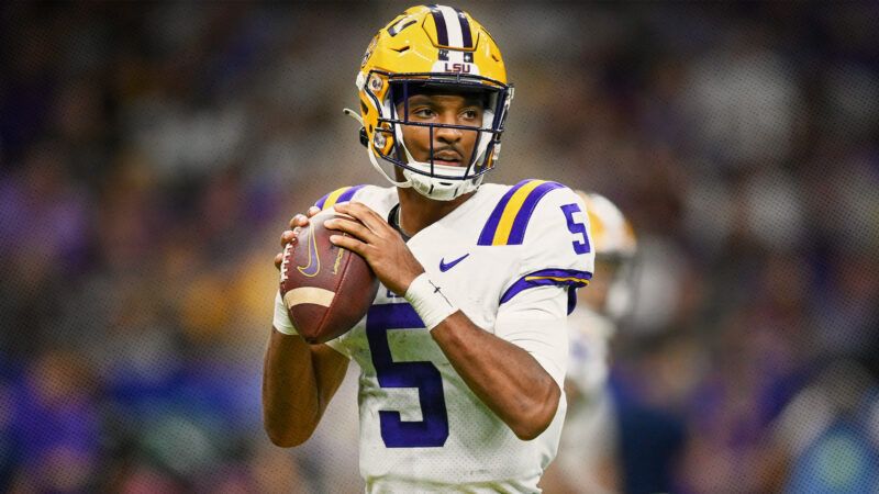 Photograph of Jayden Daniels in a white LSU football jersey (with purple and yellow stripes on the shoulders) holding a football and preparing to throw a pass. The background around him is blurred. | Photo: Kevin Langley/Icon Sportswire EHB/Kevin Langley/Icon Sportswire/Newscom