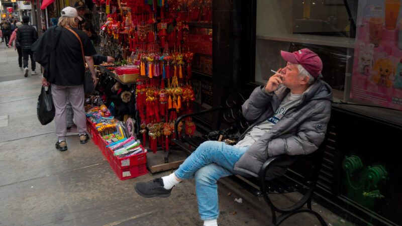 A man sitting on a chair on the sidewalk smoking a cigarette | Photo: Jimin Kim/ZUMAPRESS/Newscom