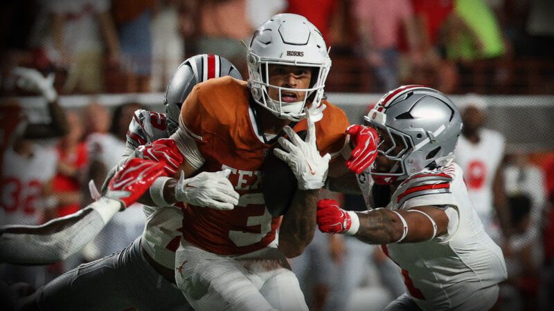 A football player in an orange Texas jersey holds the ball and tries to escape a few players in white Ohio State football jerseys that are trying to tackle him. | David Buono/Icon Sportswire DCV/David Buono/Icon Sportswire/Newscom