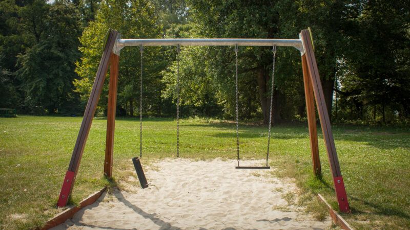A swing set with two swings, one of which has a broken chain. | Dennis Van De Hoef/Dreamstime