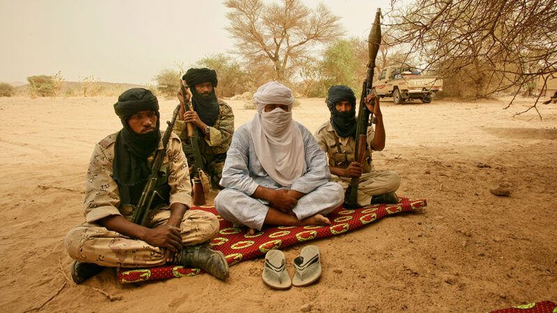 A group of men with head coverings and weapons sit on a run | Photo: Iyad Ag Ghali; Patrick Robert/Corbis/Getty