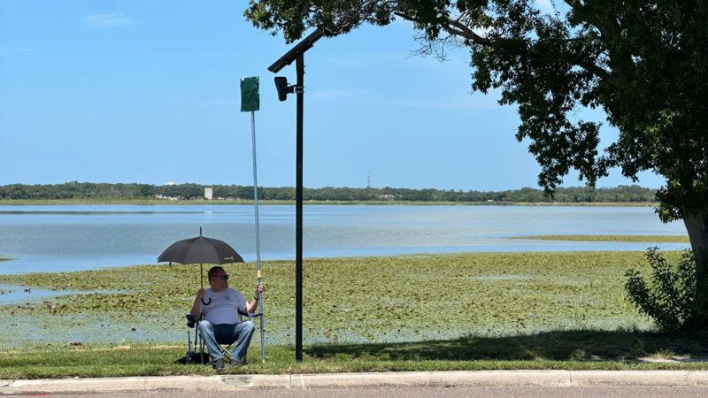 A man sitting in a lawn chair hoists a small placard to obscure a surveillance camera | Photo: Valerie Smith/Creative Loafing Tampa Bay