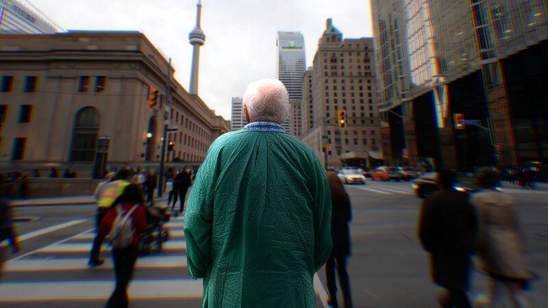 An elderly man with white hair stands on a sidewalk in a green hospital gown with the CN Tower in the background. | Illustration: Adani Samat/Midjourney. Photo: Nadtochiy/Dreamstime