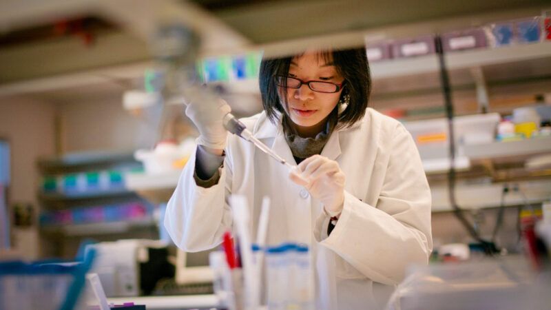 A photo of a woman in a white labcoat injecting something into a small clear tube. | Photo: Tommy Song/Dreamstime