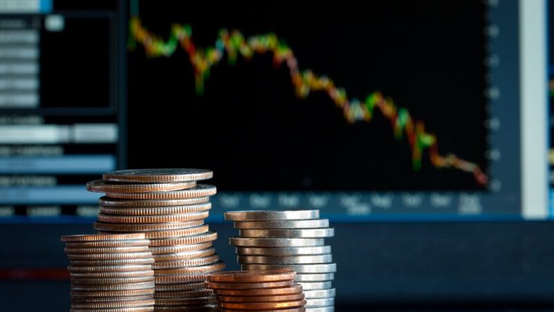 A stack of coins in front of a graph of a financial market going down. | Kenishirotie/Dreamstime