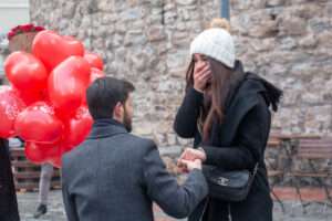 A man, down on one knee, proposes to a stunned woman.