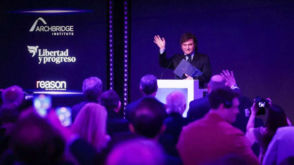 Javier Milei waves to the crowd from a lectern at a conference