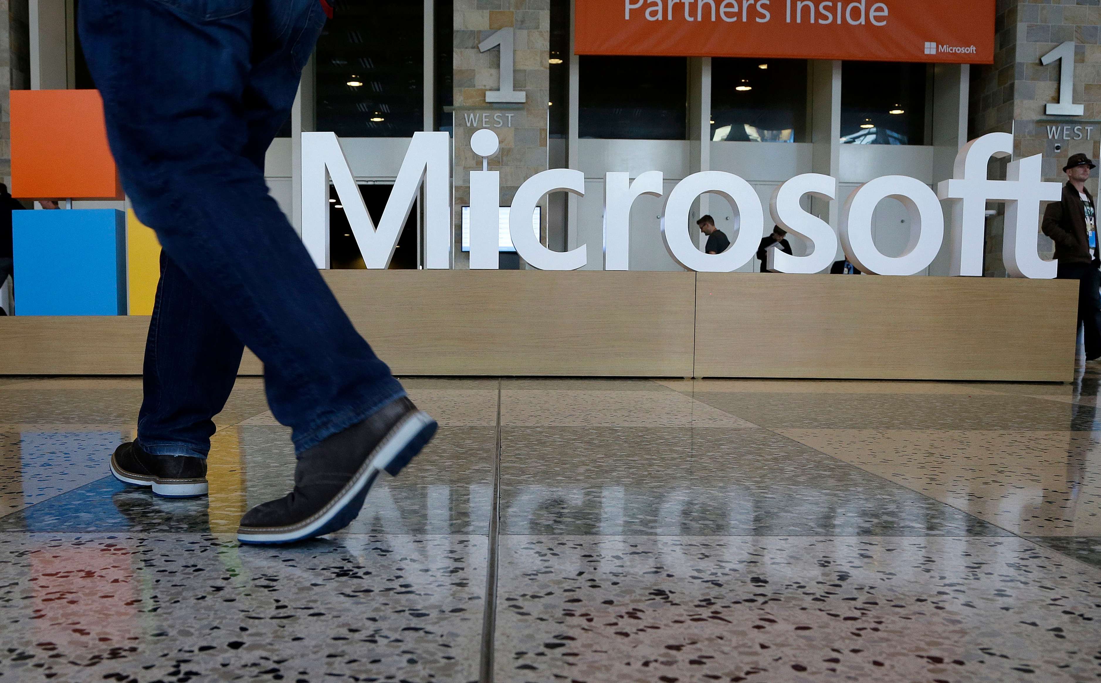 In this April 28, 2015 photo, a man walks past a Microsoft sign set up for the Microsoft BUILD conference at Moscone Center in San Francisco. Microsoft reports quarterly financial results after the market close on Tuesday, July 21, 2015. (AP Photo/Jeff Chiu)